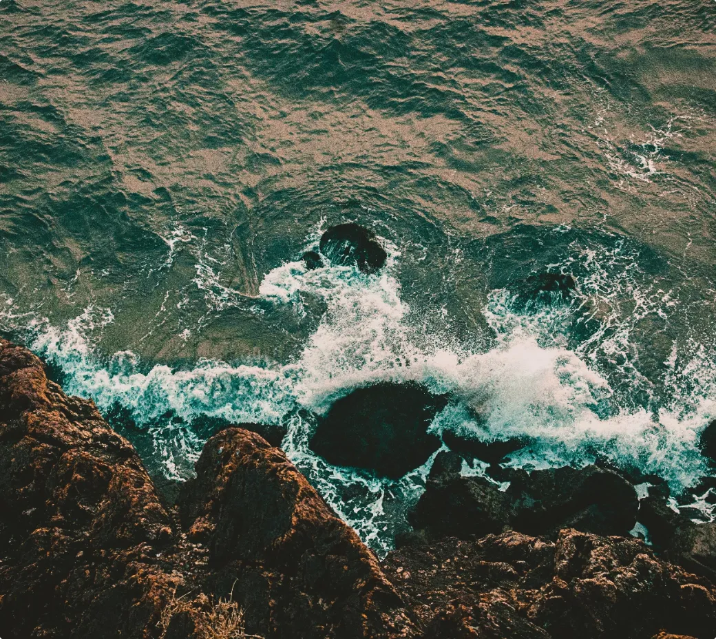 Ondas batem em rochas numa costa ao pôr do sol